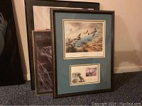 Framed D-Day 50th anniversary print and other framed posters stacked on carpet floor