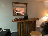Front view of wood freestanding bar with items on top, wood framed mirror in background