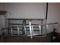 Aluminum extension ladder and folded white plastic top folding table resting against a wall