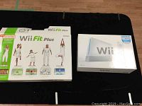 Photo of Nintendo Wii console box and Wii Fit Plus game box showing original packaging with artwork and text.