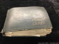 Exterior of a black, worn postcard album labeled 'Postal Cards' showing thick pages inside