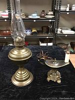 Brass oil lamp and electrified Aladdin-style lamp on black cloth surface with shelving in background.