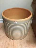 Front and side view showing ribbed design and smooth rim of clay planter on wooden floor.