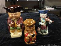 Three vintage Toby jugs displayed together on a black surface, showing front view.