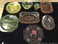 Overview of yellow and pink Depression Glass pieces arranged on black surface, showing all plates, trays and bowls in the lot