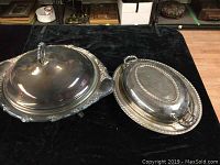 Two vintage silver plated covered casseroles with glass inserts shown from top and bottom view on dark fabric background.