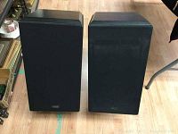 Pair of rectangular black fabric grille stereo speakers on floor, side by side