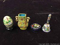 All four cloisonné items on black background: egg on stand, small vase, heart-shaped jewelry box, floral bell