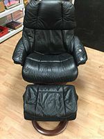 Front view of black leather lounge chair with ottoman on wooden round base