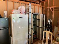Aluminum extension ladder stored vertically beside refrigerators in a garage or workshop area.