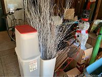 Vintage sled, storage bins, white faux branches in vase, and twinkling snowman in garage setting