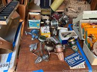 Overview of seven assorted fishing reels on tabletop including boxed and unboxed units