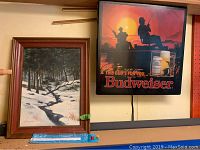 Framed wall art painting with winter forest and creek scene and electric Budweiser sign showing fishing silhouette artwork and Budweiser beer cans