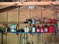 Wood shed interior showing multiple garden and fuel-related items on shelves, including plant food, lighter fluid, red gas cans, and sprayers.