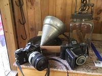 Overview of lot showing Nikkormat camera with attached lens and strap, Kodak folding camera, butter churn, rolling pin and pie molds on countertop