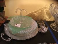 Several stacked trays: green glass ruffled edge, clear glass ruffled edge, cut glass, and an aluminum tray with handles.