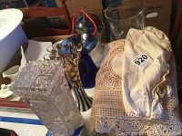 Photo showing clear cut glass vase with break, blue MacKenzie Childs vase with horse print and other glass vases, along with folded beige linens.