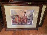 Photograph of Independence Hall framed print with mat and glass seen in wooden frame, showing street scene with people in period dress, and the historic red brick building with clock tower.