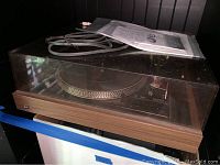 Front angled view showing the full turntable unit, dust cover, control lights, and cables on top.