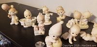 Group photo showing 10 Precious Moments porcelain figurines in various playful poses on a dark surface with a white wall background.