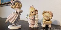 Three Precious Moments porcelain figurines from 1999, 2002, and 2003 photographed to show details and colors.