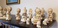 Front angled view of the full set of Precious Moments nativity figurines on a dark shelf including Mary, Joseph, Baby Jesus, 3 Wise Men, shepherd, angel, and animals.