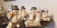 Group photo of seven Lenox snowmen Christmas figurines showing various poses and festive accessories including gifts, lantern, candy canes, and sleigh with dates 2001 and 2005 visible.