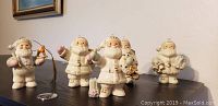 Five Lenox Santa figurines displayed on a surface, each holding different holiday items with gold accents, showing front views.