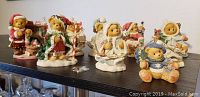 Eight Cherished Teddies Christmas-themed figurines displayed on a dark shelf against a white wall. The figurines show teddy bears in various holiday poses and attire.