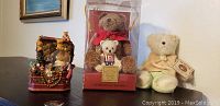 Photo showing Lenox 100th Anniversary Bear music box in packaging alongside Boyd's stuffed bear with tag, placed on a table with framed picture in background.