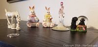 View of all figurines arranged on shelf including two unicorns, two bunnies, black dog snow globe, and crystal dress form.