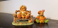 Photo of two Cherished Teddies fall-themed figurines on a black surface against a white wall.