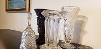 Photo showing four crystal vases and one crystal bell arranged on a surface, highlighting different shapes and colors including a dark red vase and clear crystal pieces.