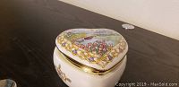Heart-shaped porcelain music box closed, showing detailed floral artwork and gold trim on lid.