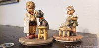 Two Hummel porcelain figurines, one boy doctor with dog and one girl nurse with dog, displayed on a surface.