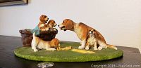 View of dog family figurine from front showing puppies in basket and two larger dogs on green base.