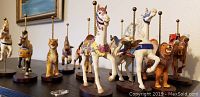 Set of 12 animal carousel figurines displayed on a surface, showing various animals including horses, tigers, lion, camel with attached poles on bases.