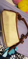 Side view of beige Dooney & Bourke shoulder bag showing fabric body and brown leather strap with buckle