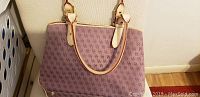 Front view of the Dooney and Bourke handbag showing purple logo canvas and beige leather handles.