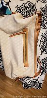 Show front side of the beige monogram printed Dooney & Bourke bag with exterior zip pocket and tan leather accents.