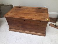 Front view of antique pine blanket box on carpeted floor showing natural wood finish and signs of wear