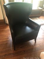 Front three-quarter view showing black leather upholstery, wingback design, and armrests.