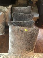 Front view of four gray plush pillows showing soft faux fur-like textured covers and some wear