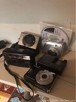 Overview of multiple cameras including Sony Cyber-shot, Canon digital and film cameras, Nikon Coolpix, and an installation CD disk.