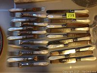 Photo showing all 12 forks and 11 knives arranged on a surface, highlighting the mother of pearl handles and metal blades with decorative engravings.