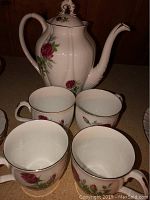 Coffee pot displayed with four matching cups on countertop