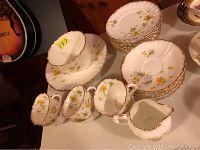 Top view of dish set components including the punch bowl, cups, plates, and saucers with yellow floral pattern and gold-trimmed scalloped edges
