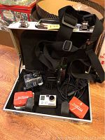 Open metal carry case showing GoPro Hero camera, batteries, straps and cables.