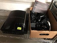 Sony PlayStation 3 black console with box of accessories including controllers and cables.