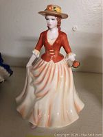 Front view of Royal Doulton Autumn Stroll porcelain figurine showing woman in orange and cream dress with hat and flowers.